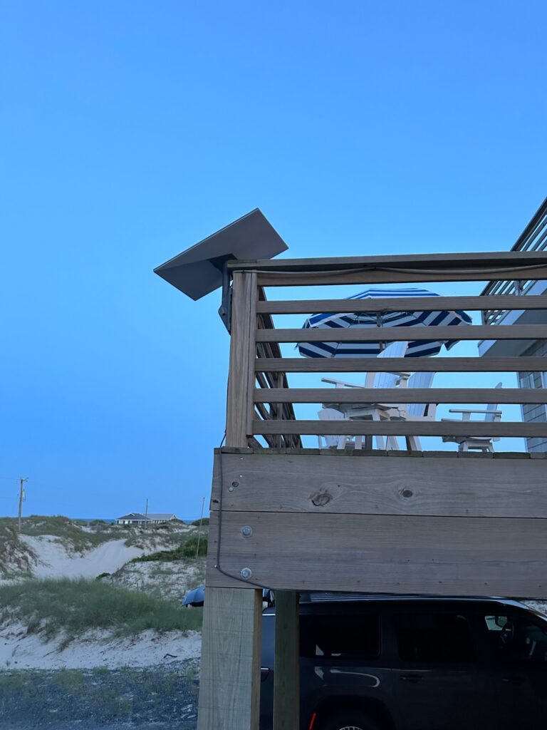 Satellite dish mounted on wooden deck corner post of a beach house near the dunes — 4x4 beach area, Outer Banks